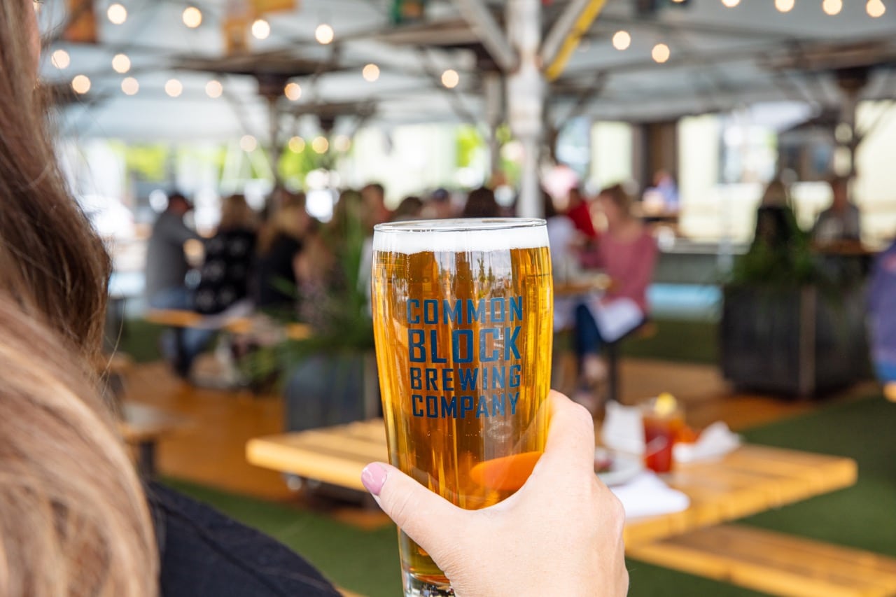 A person holds a beer labeled with Common Block Brewing Company.
